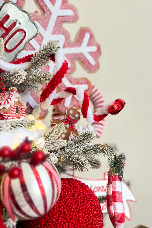 A close-up of a portion of the Christmas tree showcases the intricate details of the ornaments. We see snowy branches intertwined with red and white candy canes. The central focus is on a silver "HO" ornament, surrounded by red snowflakes and furry white trim. In the backdrop, other decorations like gingerbread men and white baubles are visible.