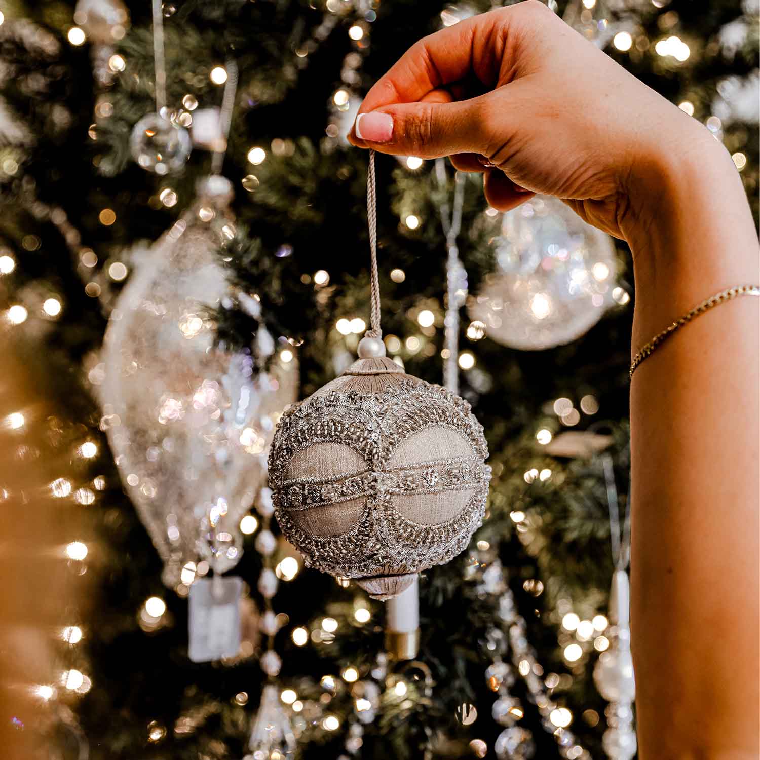 Hand placing luxury Christmas ornament on tree, sparkling with christmas tree decorations Sydney and elegant christmas ornaments.