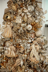 Close-up of a section of the Christmas tree showcasing detailed ornaments. Angels, sparkling globes, and golden starbursts can be seen prominently against a backdrop of green pine needles.