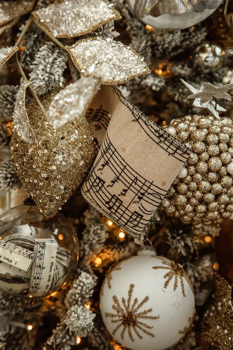 Another close-up of the tree's decorations, capturing a crystal-clear bulb ornament with intricate designs. Nearby is a golden, sparkling leaf decoration. A blurred shadow of a star ornament is cast on the background.