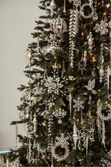 A detailed view of a Christmas tree adorned with intricate silver ornaments, crystal droplets, and twinkling lights, showcasing the tree's elegance and festive charm.