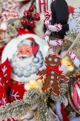 An even closer view of the Christmas tree's ornaments, highlighting their textures and colors. The focal point is a shiny red and white striped bauble, accented with holly berries on top. It's nestled among snow-dusted pine branches and neighboring ornaments, including a red beaded sphere and a gingerbread man.