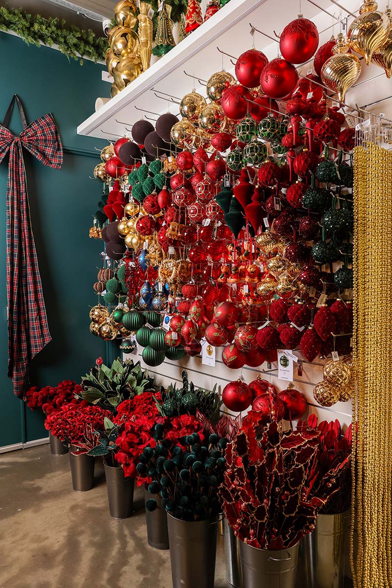 Wall of red and gold Christmas ornaments above potted red florals in the Dancer & Dasher Christmas decoration shop