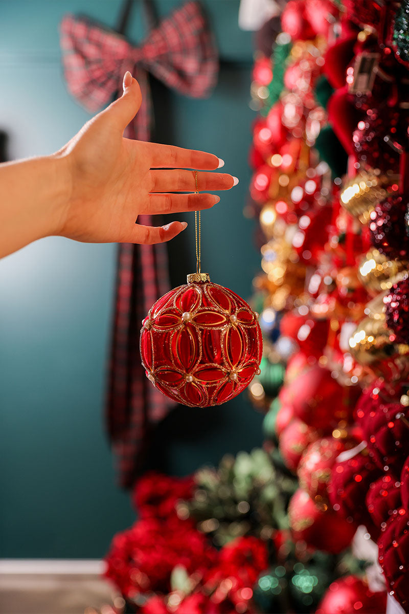 Hand reaching for a red and gold glass bauble hanging in front of a wall of Christmas ornaments