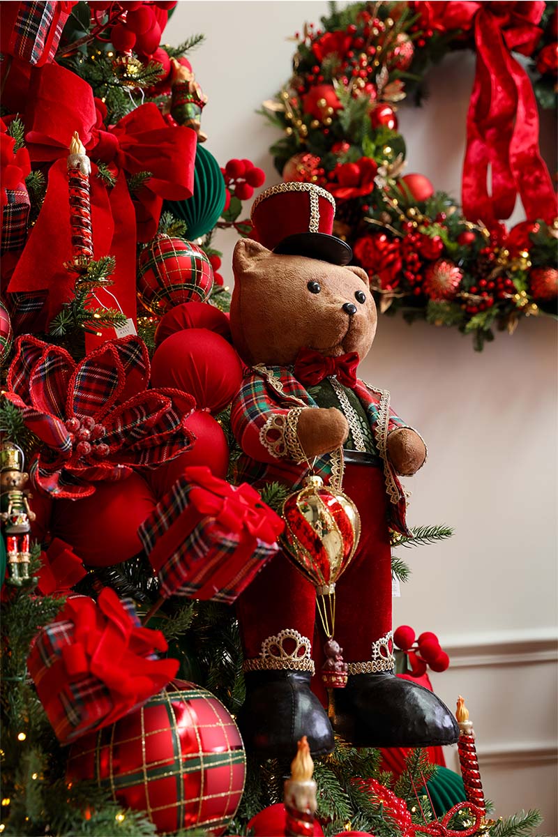 Teddy bear in tartan beside a red berry tree and wreath, a festive display at the Dancer & Dasher Christmas shop
